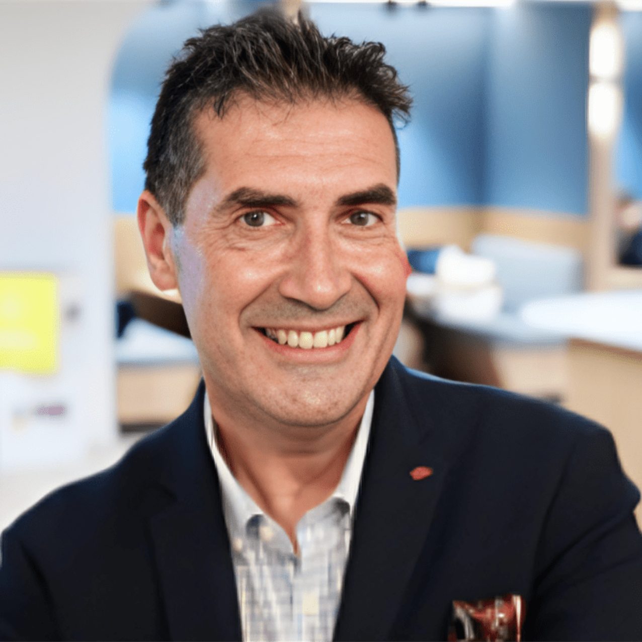 Smiling man in a blazer posing in an office setting.