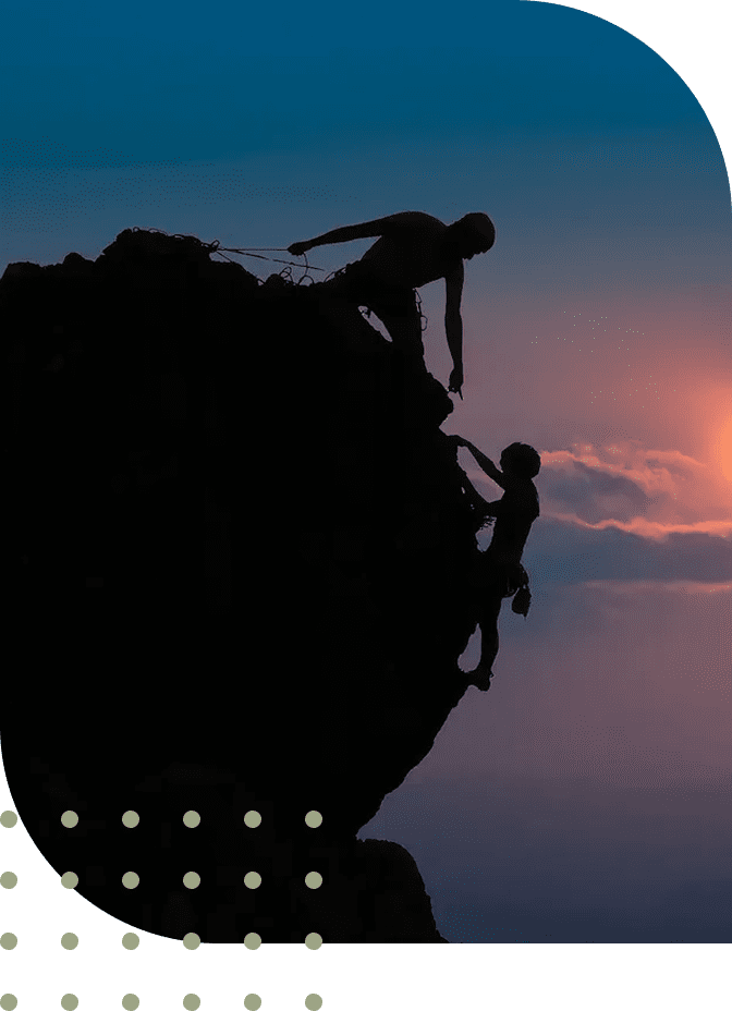 Two climbers helping each other ascend a steep rock at sunset.