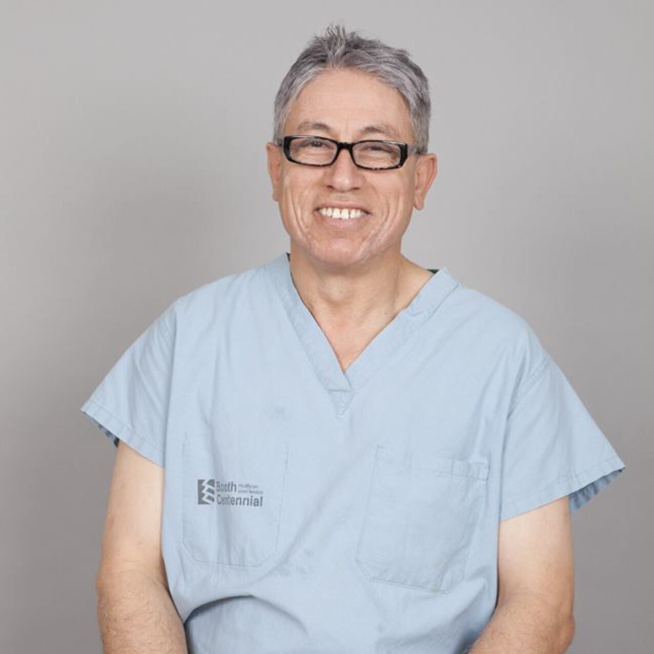Smiling healthcare professional in blue scrubs and glasses.